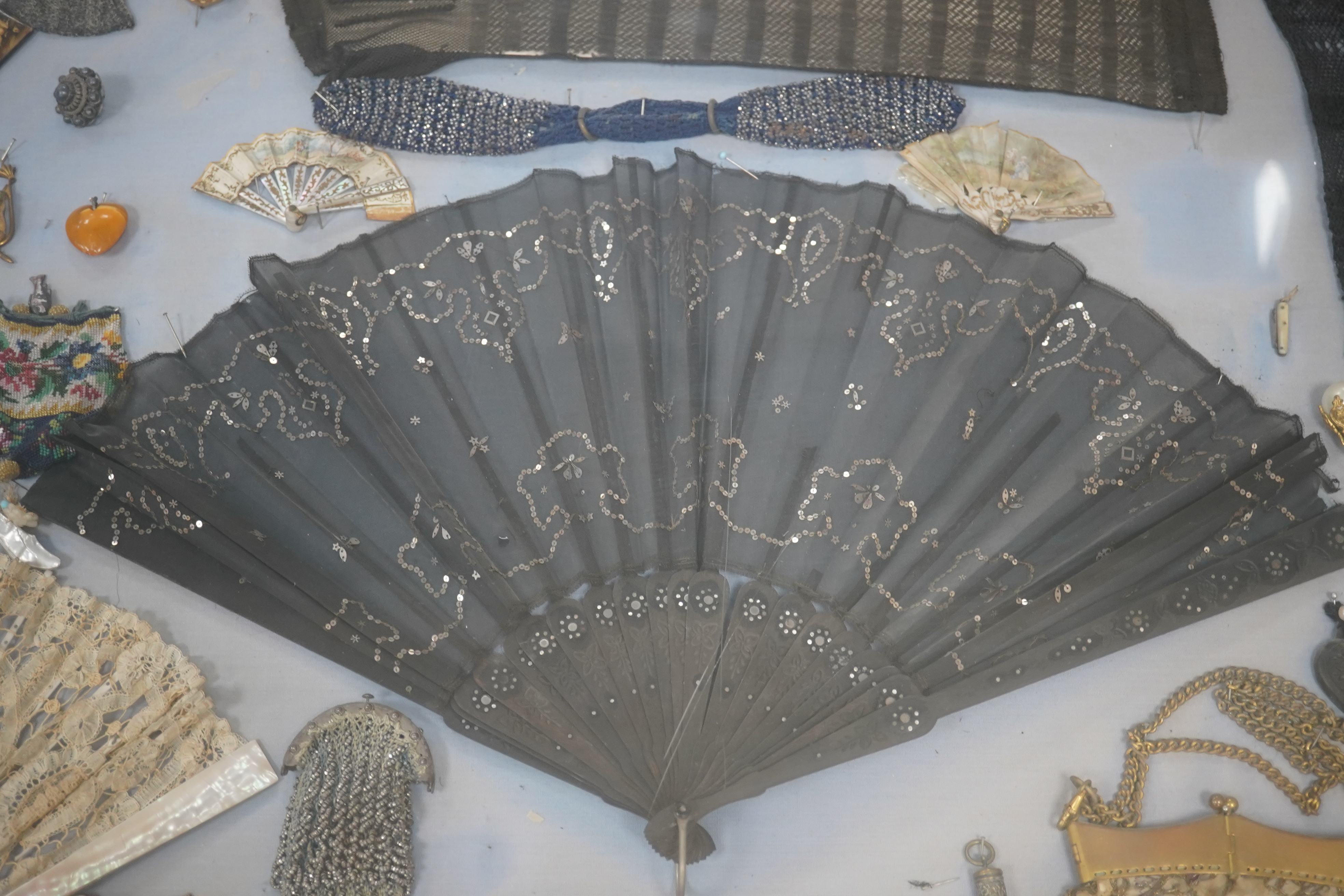 A framed display montage of late 18th and 19th century decorative ladies sequin and lace fans, beadwork reticules, cut steel misers purses, hat pins, earrings, brooches, shoe buckles and crochet mittens.100cm x 70cm. Con